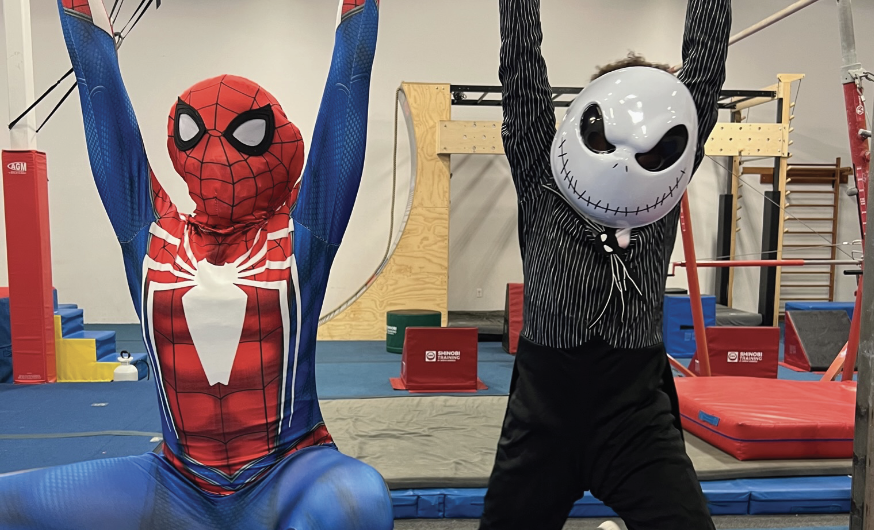 Kids in a spider-man costume and Jack Skellington costume hanging from a gym bar